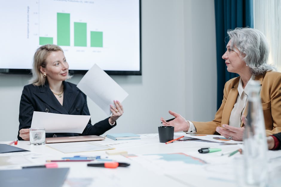 Two businesswomen engaged in a meeting discussing charts in an office setting.